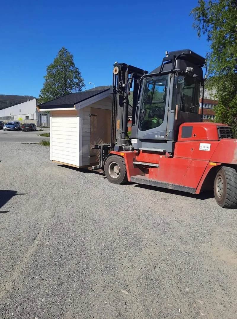 Gaffeltruck ved et lite trebygg